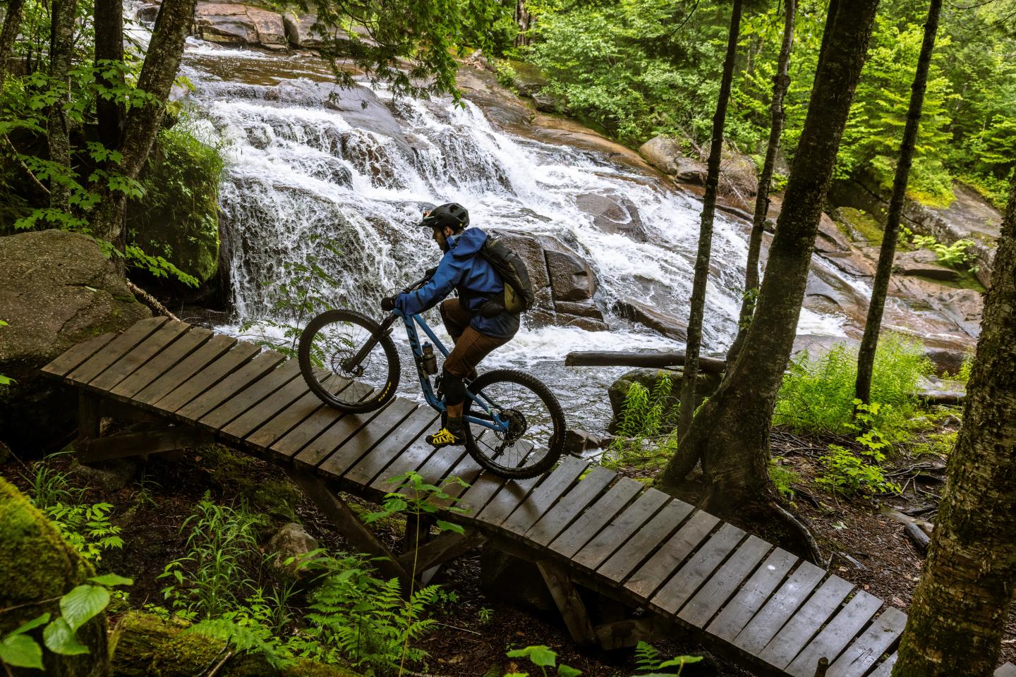 Vélo sur passerelle en bois devant une cascade en forêt verdoyante.