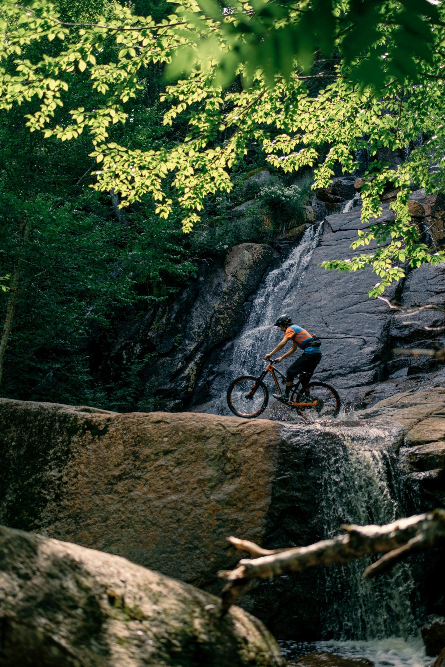 Cycliste sur un sentier rocheux près d'une cascade en forêt.