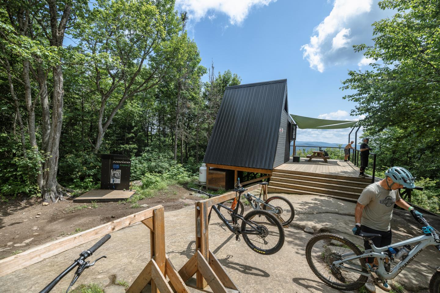 Un cycliste près d'un abri moderne en bois dans une forêt ensoleillée.