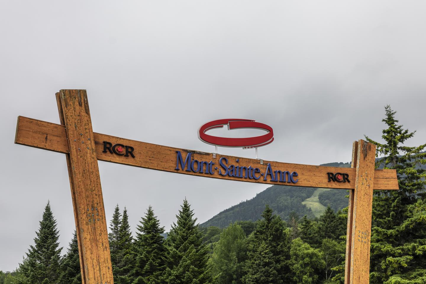 Entrée en bois du Mont-Sainte-Anne, arbres et ciel nuageux en arrière-plan.