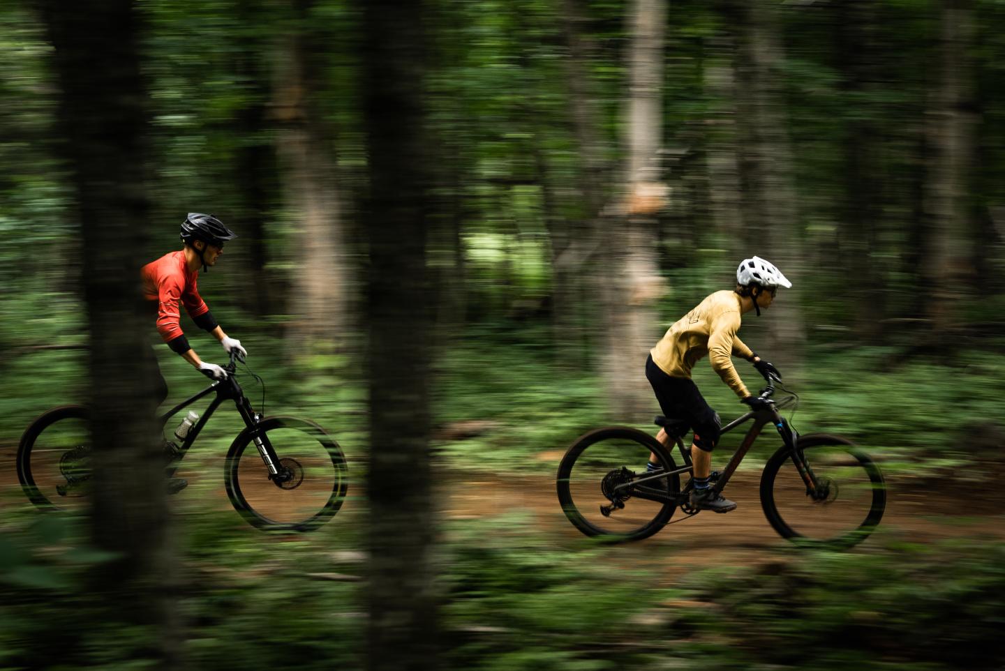 Cyclistes en forêt sur un sentier, portant des tenues rouge et jaune.